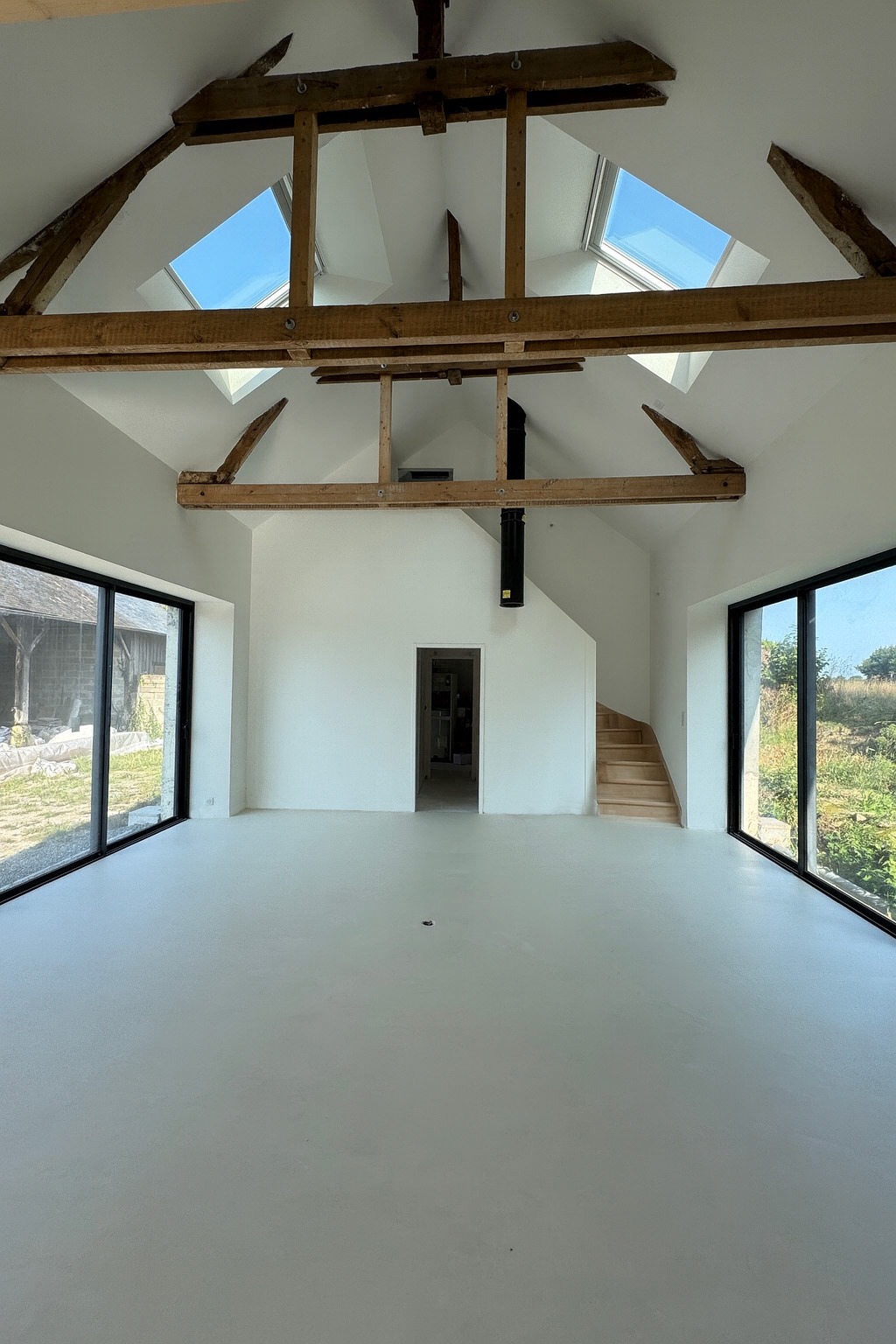 Intérieur après rénovation : grandes baies vitrées qui ouvrent la maison sur le jardin, inondant les pièces de lumière.