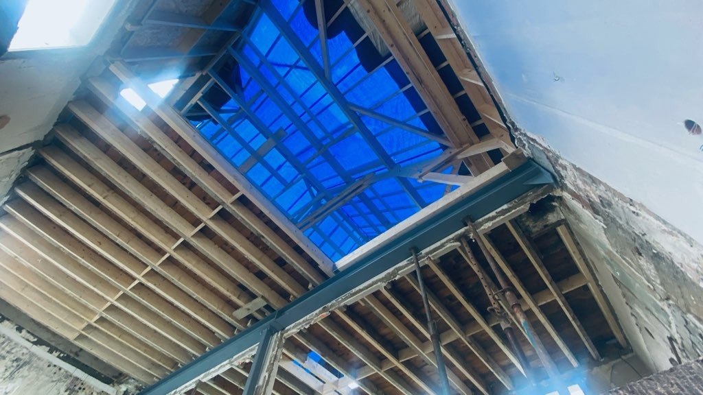 Rénovation structurelle : intérieur de la maison en chantier avec charpente bois et bâche de protection bleue